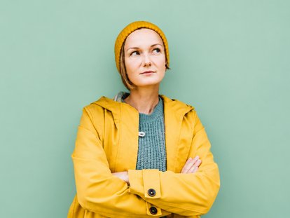 Porträt einer Frau in gelber Jacke und gelber Mütze vor smaragdgrünem Hintergrund.