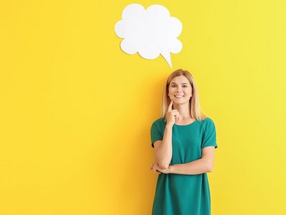 Eine Frau steht vor einer gelben Wand und lächelt. Über ihrem Kopf befindet sich eine weiße Sprechblase. Sie trägt ein türkisfarbenes Kleid und hält nachdenklich eine Hand ans Kinn.